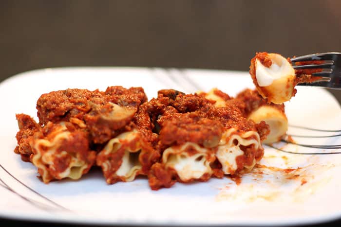 baked cheese lasagna roll-ups on a plate with bite on fork