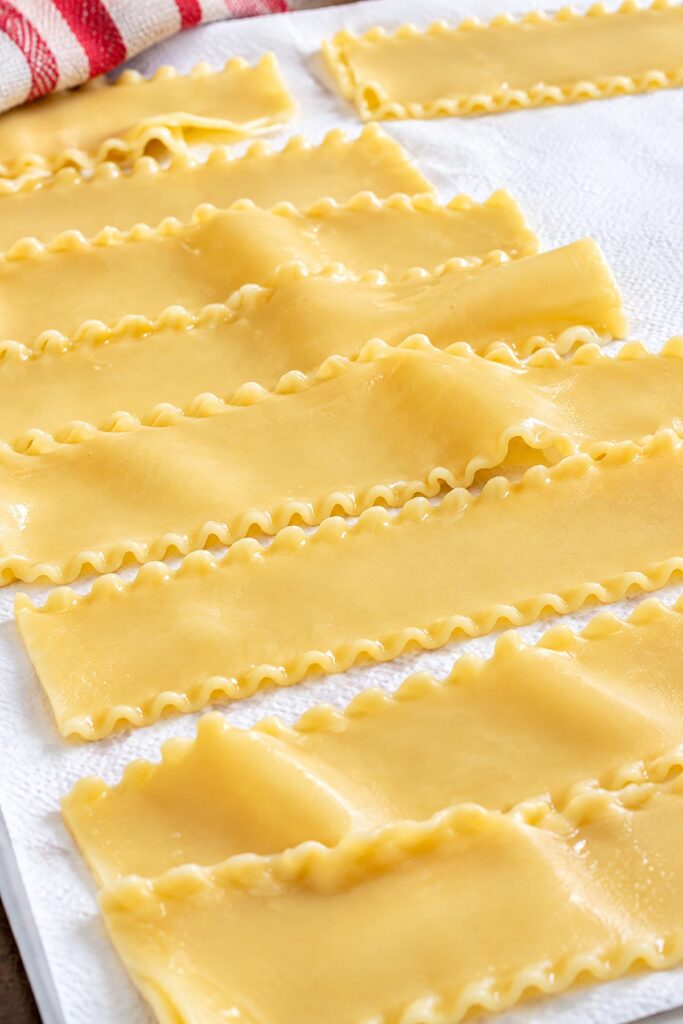 Cooked lasagna noodles laid flat on white paper towels to dry before assembling homemade lasagna rolls with cheese and sauce.