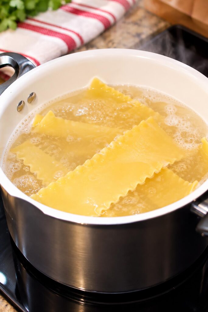 Wide lasagna noodles boiling in a large pot of water on the stovetop, showing how to cook pasta for homemade lasagna roll-ups.