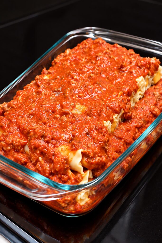 Two layers of homemade Velveeta lasagna roll ups topped with hearty meat sauce in a glass baking dish, fully assembled and ready to bake.