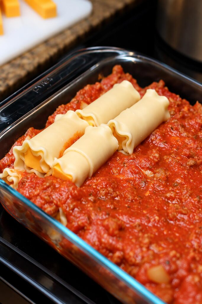 Adding a second layer of cheese-stuffed lasagna roll ups over homemade meat sauce in a glass casserole dish.
