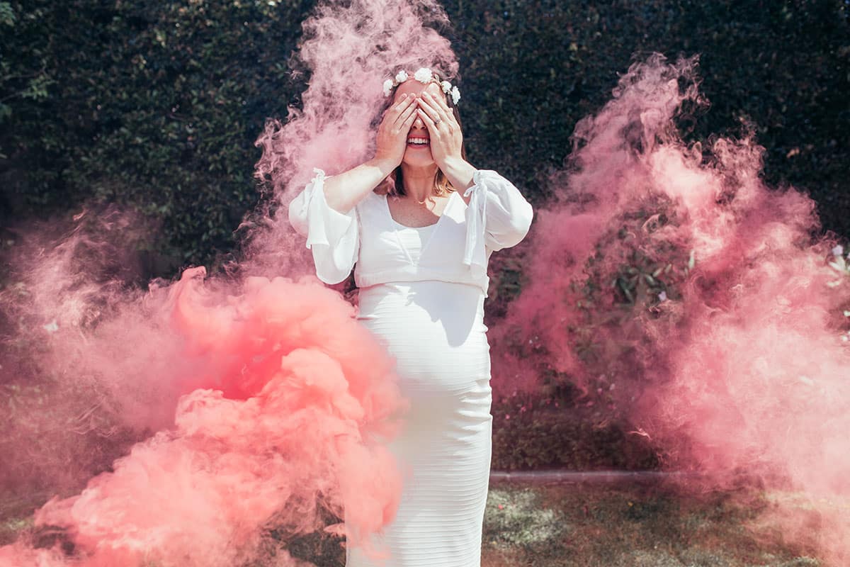 pregnant woman at gender reveal in pink smoke cloud covering her eyes