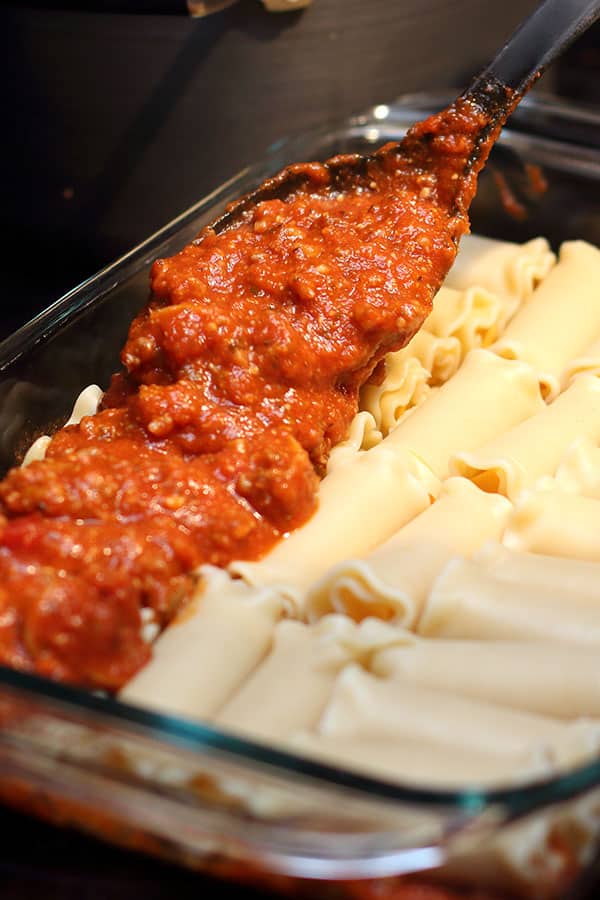 spooning pasta sauce over layer of cheese lasagna roll-ups