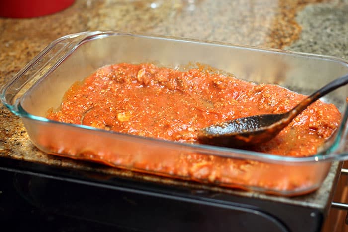 spreading thin layer of lasagna sauce in glass baking dish