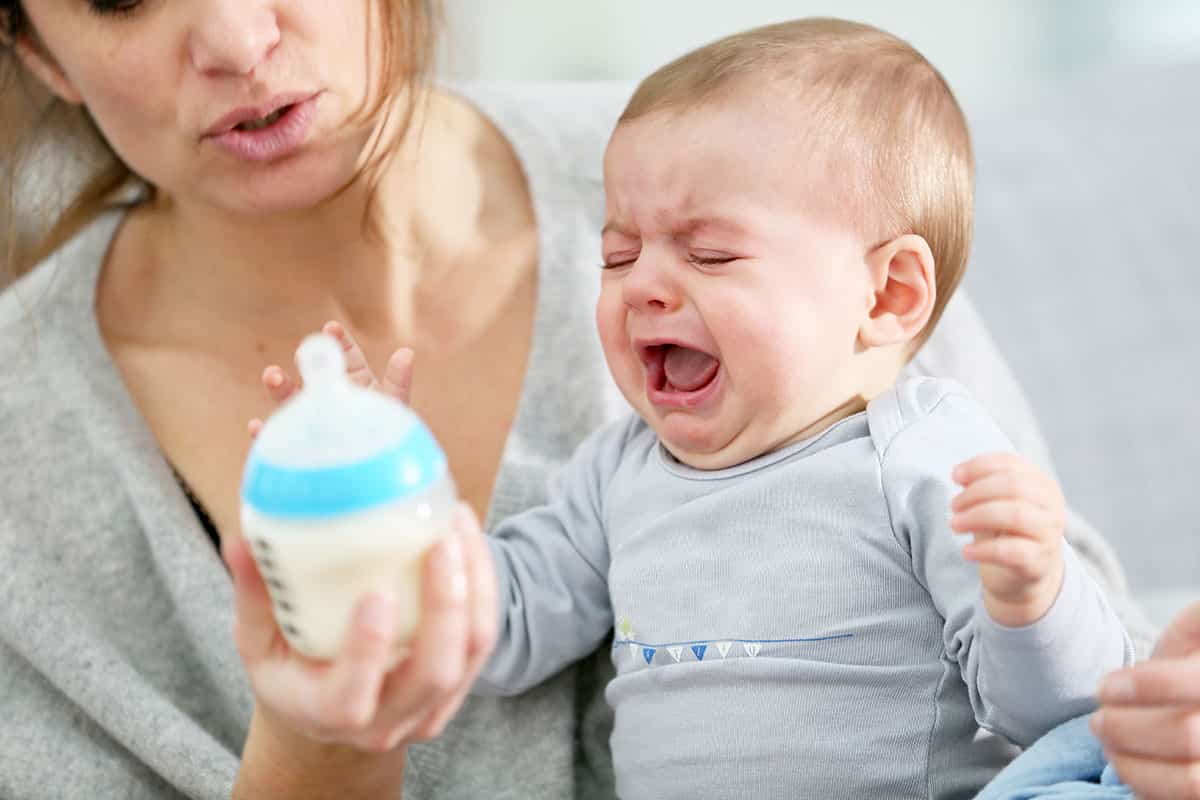 baby with colic crying at botle