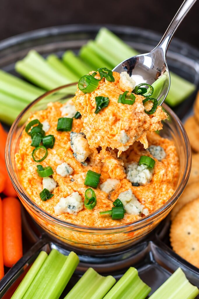 Creamy buffalo chicken dip topped with blue cheese crumbles and green onions, with a spoonful lifted above the bowl.
