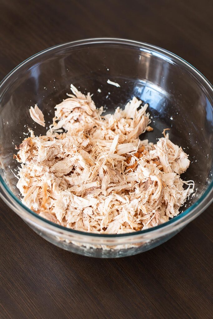 Shredded rotisserie chicken in a clear glass mixing bowl, ready to use in an easy homemade buffalo chicken dip recipe.