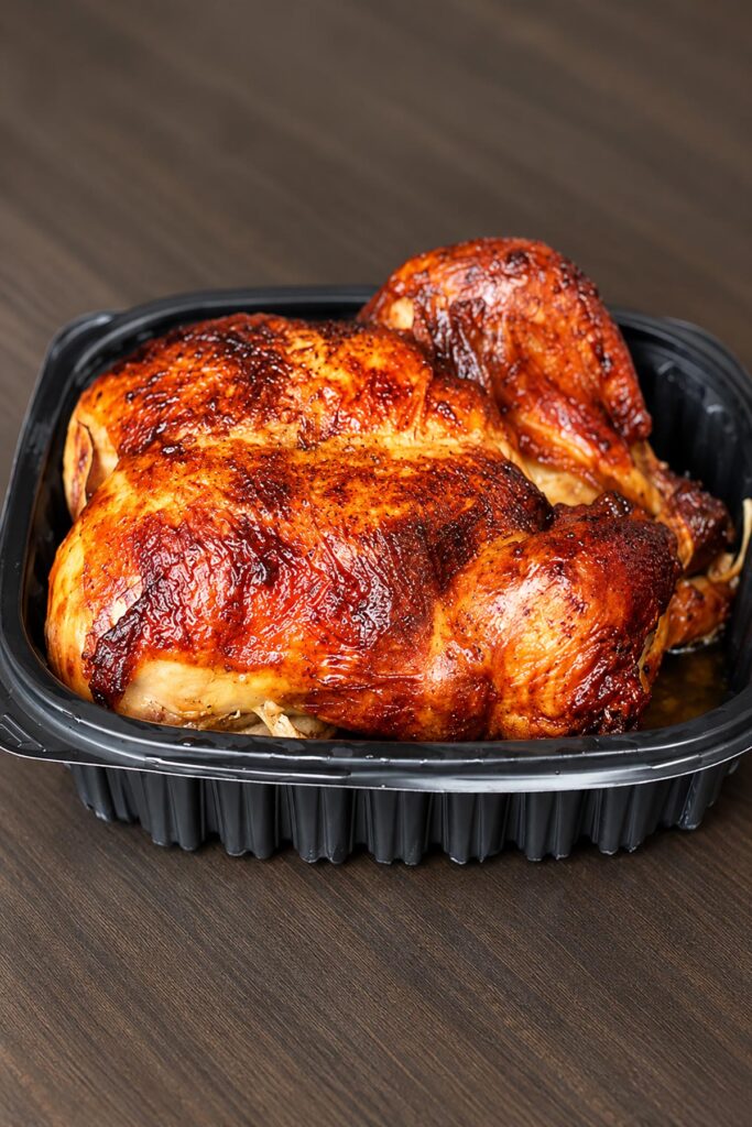 Whole golden-brown rotisserie chicken with crispy seasoned skin in a black tray, ready to shred for buffalo chicken dip.