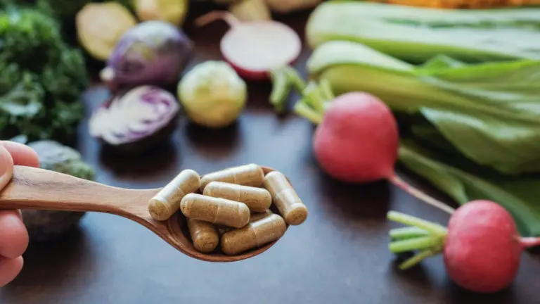 fertility supplements on a wooden spoon with vegetables and herbs in the background