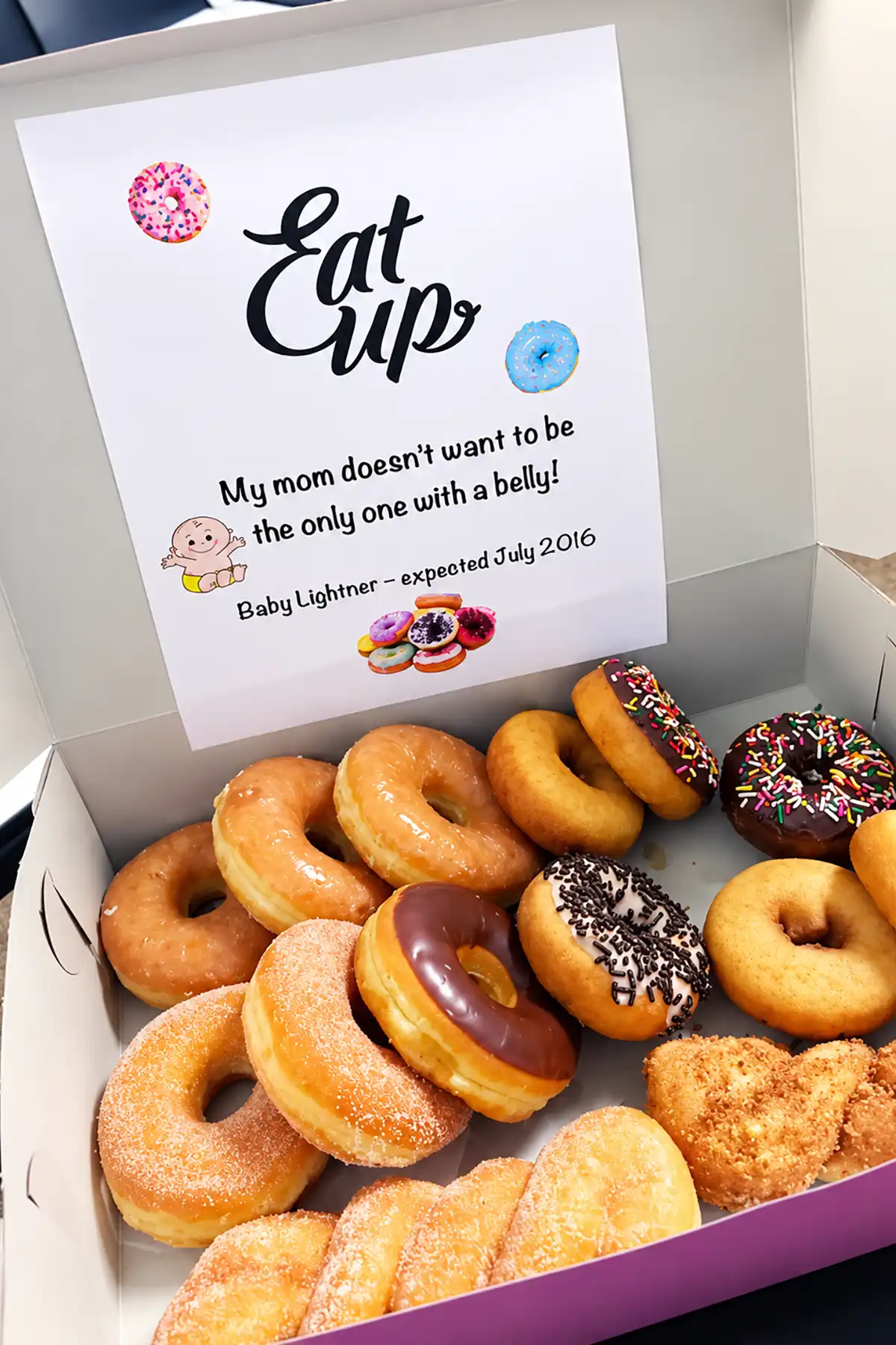 Box of assorted donuts with an Eat Up pregnancy announcement sign revealing Baby Lightner is expected in July 2016.