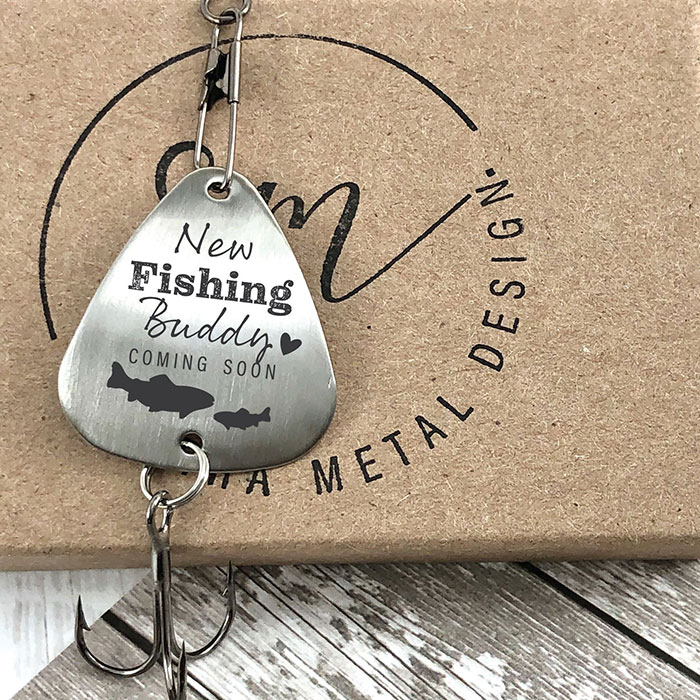 a fishing lure engraved to read "new fishing buddy coming soon" with a large and small fish
