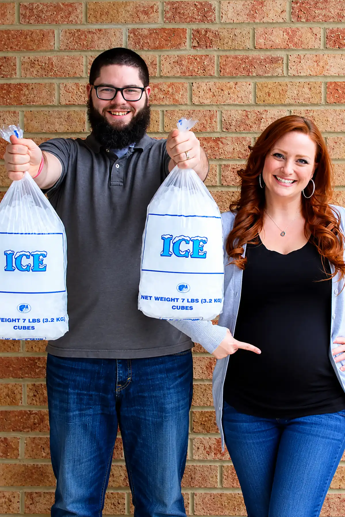Couple posing with two bags of ice against a brick wall for a funny Ice Ice Baby pregnancy announcement.