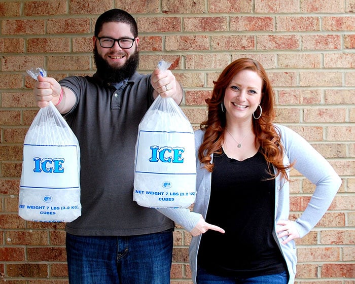 a man holding two bags of ice next to a woman pointing to her stomach