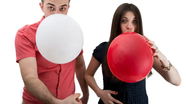 a man and woman blowing up white and red balloons, respectively, while pointing at her stomach to illustrate the metaphor for being pregnant