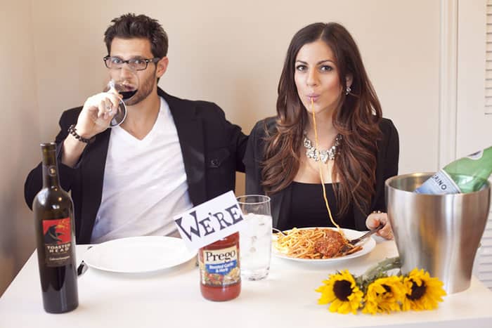 couple sitting at a table, the man drinking wine and the woman eating spaghetti with a jar of Prego sauce and the word "we're" taped above the brand name