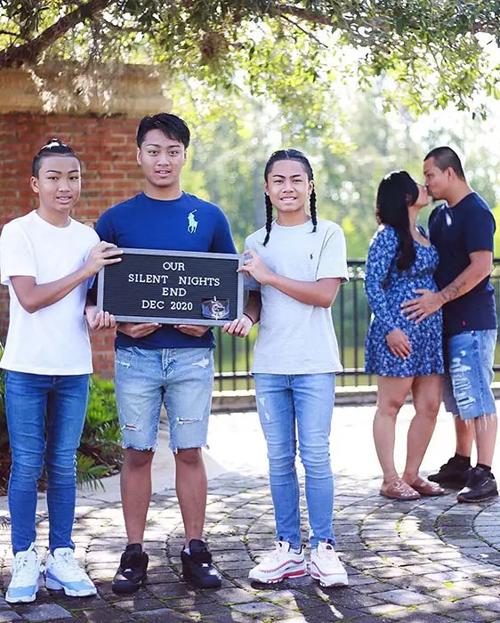 couple kissing in the background while kids in foreground hold a letter board that reads "our silent nights end Dec 2020"