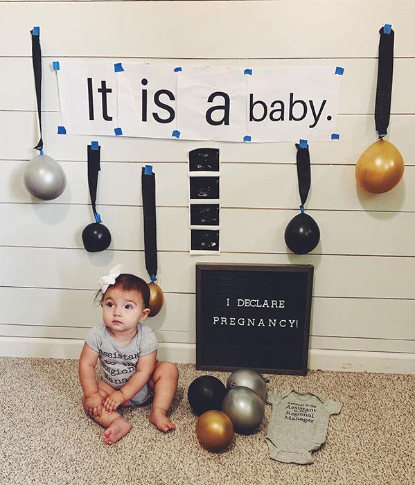 a baby sitting next to black, silver, and gold balloons with a letter board that reads "I declare pregnancy!"