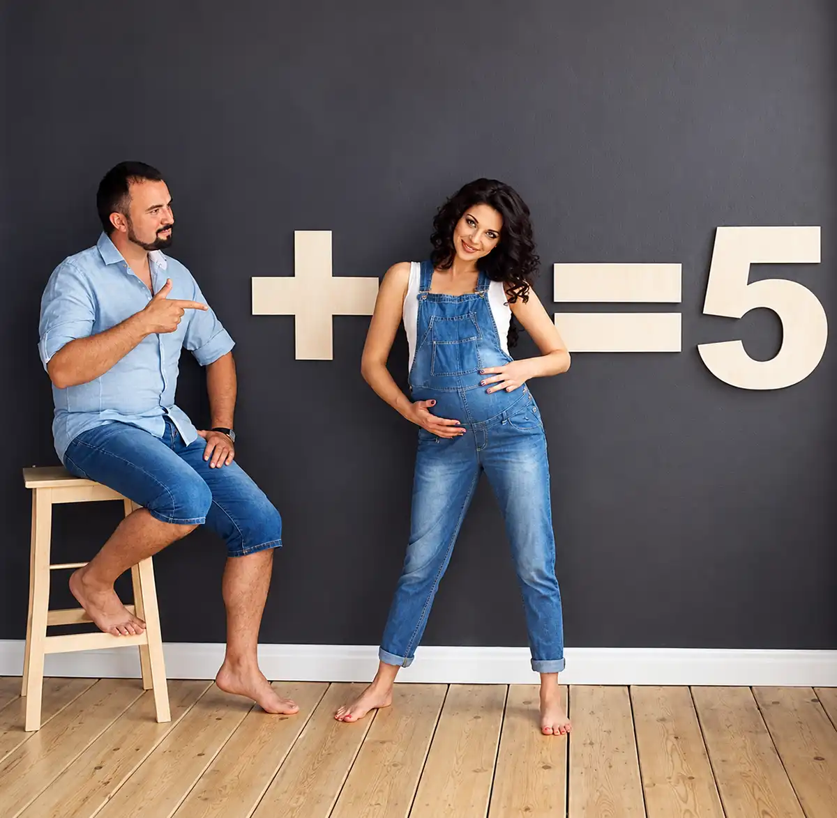 Couple announcing triplets with a pregnancy math equation showing a plus sign and equals five against a dark wall.