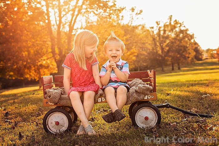 two young children brother and sister sitting on wagon in sunset fall family photo
