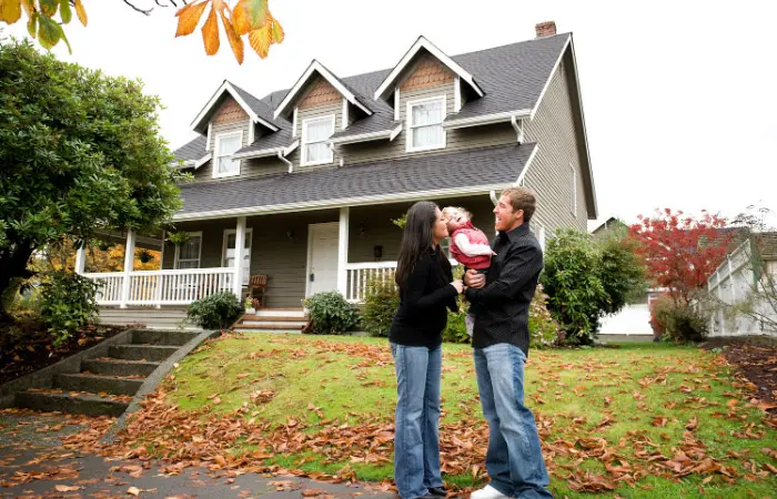 couple with baby taking fall family photos outside their home