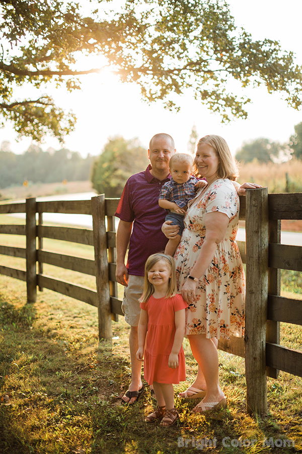 family of four with plus size mom standing by fence in the fall