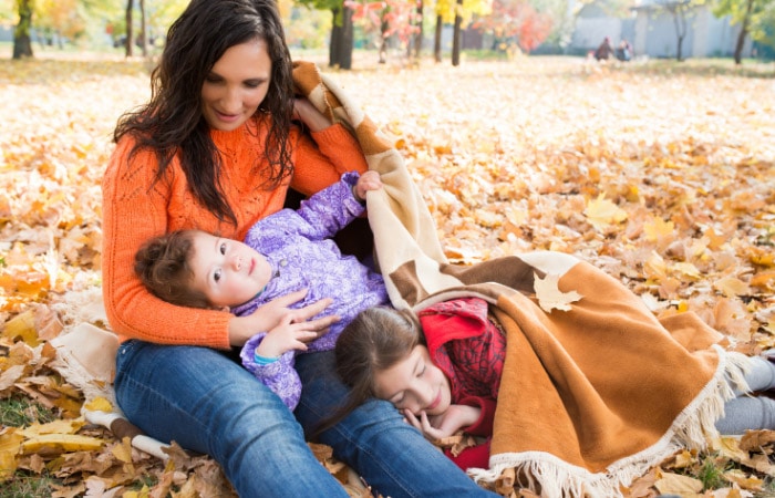 mother and two daughters lying in leaves in the fall