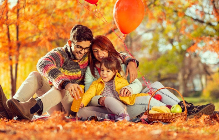 family of three sitting in autumn leaves in the fall, orange aesthetic