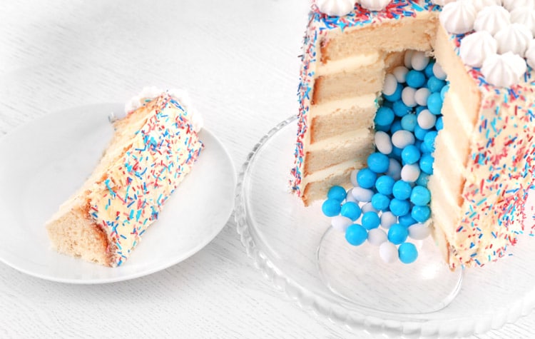 five-layer round white cake covered in rainbow sprinkles cut open to reveal blue and white round candies inside for a boy gender reveal