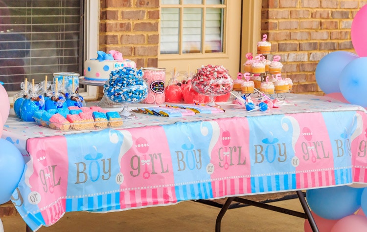 a gender reveal dessert table decorated in pink and blue with balloons on the sides