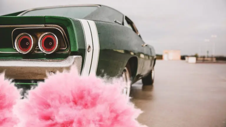 the rear of a muscle car blowing pink smoke out behind it