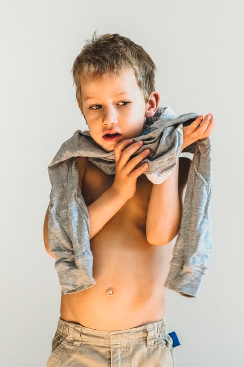boy trying to take off a long-sleeve shirt that's too small