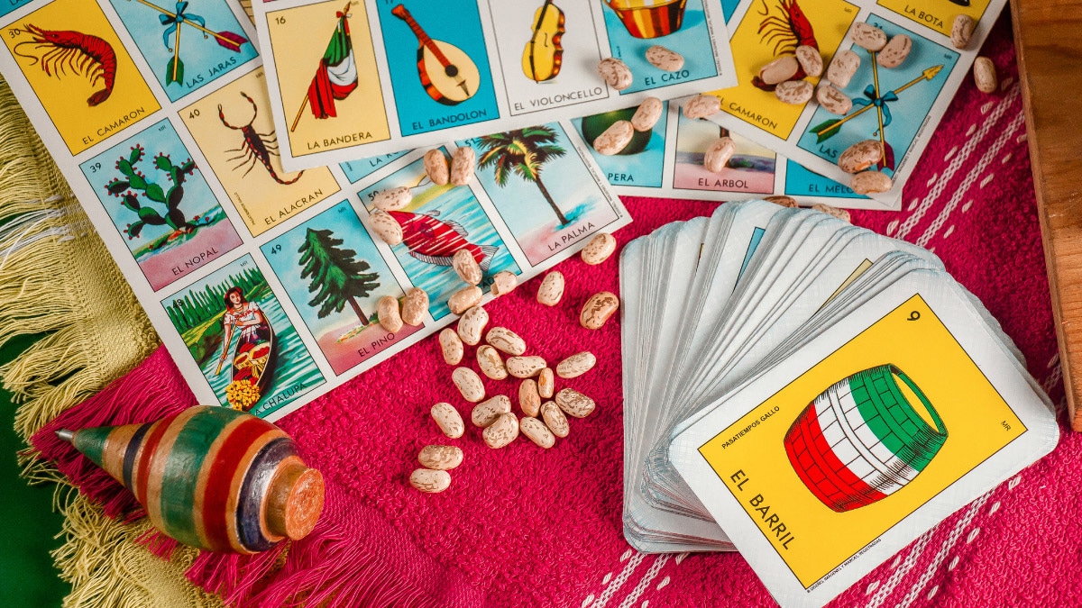 a table covered in Mexican loteria cards, beans, and a maraca