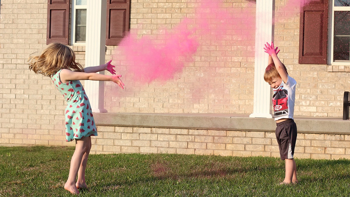 two young children throwing pink color powder in the air outside their home