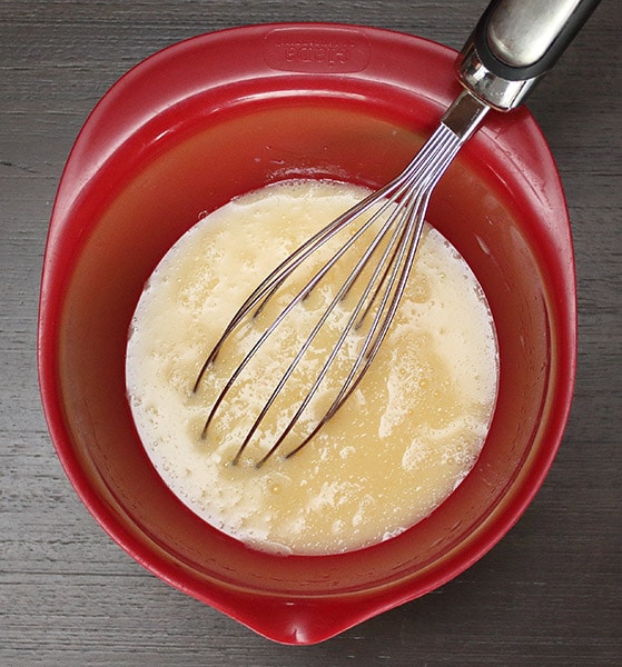 eggs, milk, vegetable oil, and vanilla extract in a red mixing bowl with a whisk