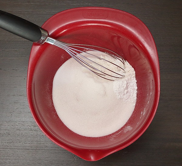 flour, sugar, baking powder, and salt in a red mixing bowl with a whisk
