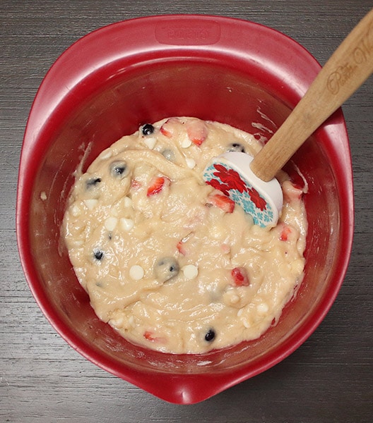 fruit mixed into muffin batter in a red mixing bowl