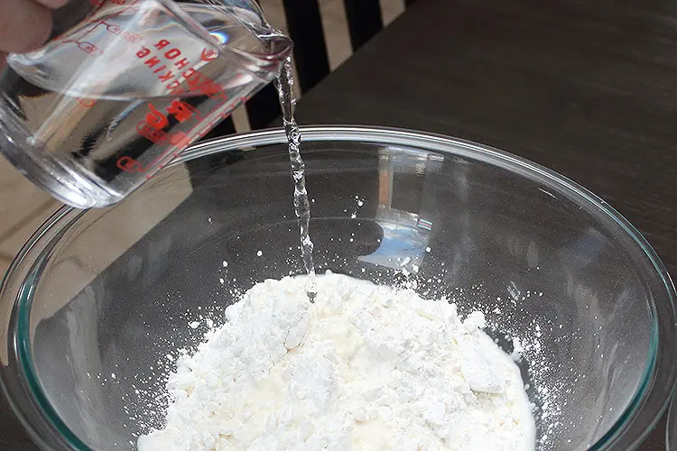 water being poured into a glass bowl filled with cornstarch