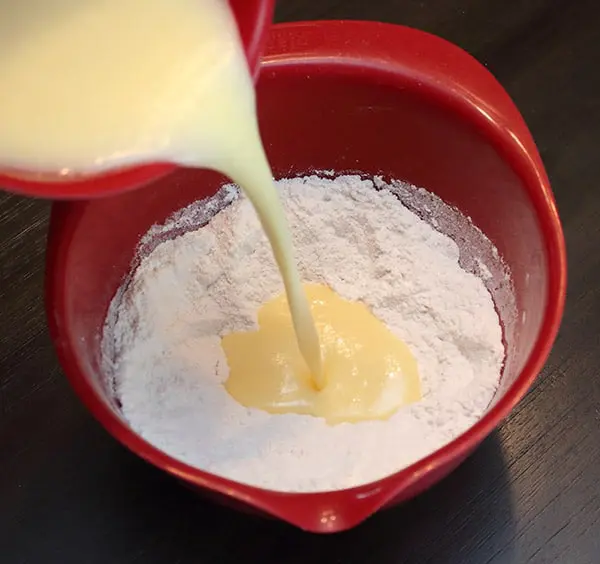 wet ingredients being poured into dry ones in a red mixing bowl