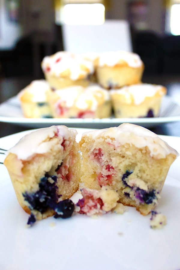 a red, white and blue muffin cut open in the foreground with a plate stacked with muffins in the background