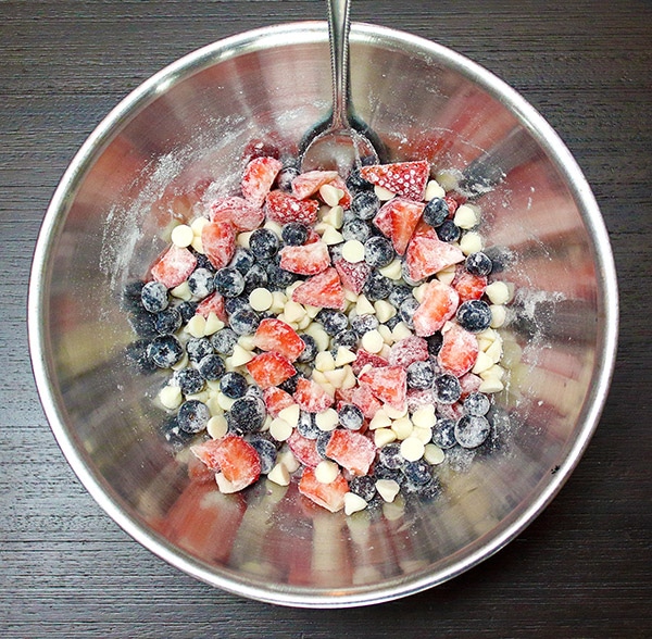 strawberries, blueberries, and white baking chips tossed in flour in a metal bowl