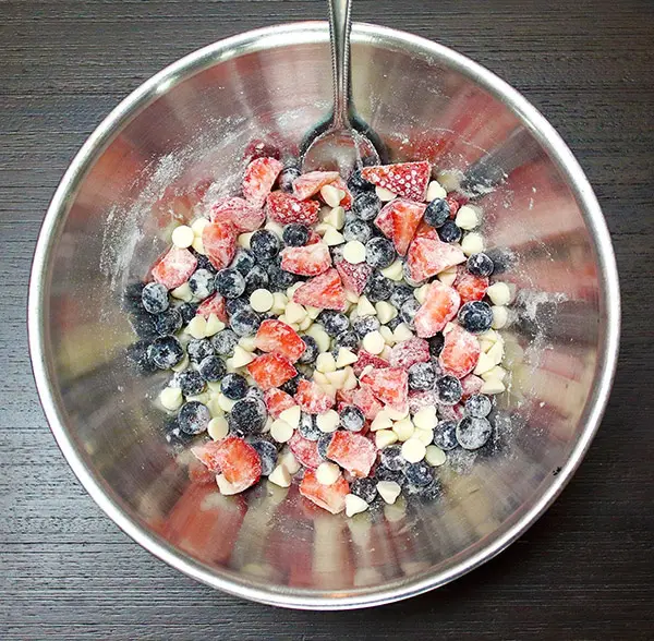 strawberries, blueberries, and white baking chips tossed in flour in a metal bowl