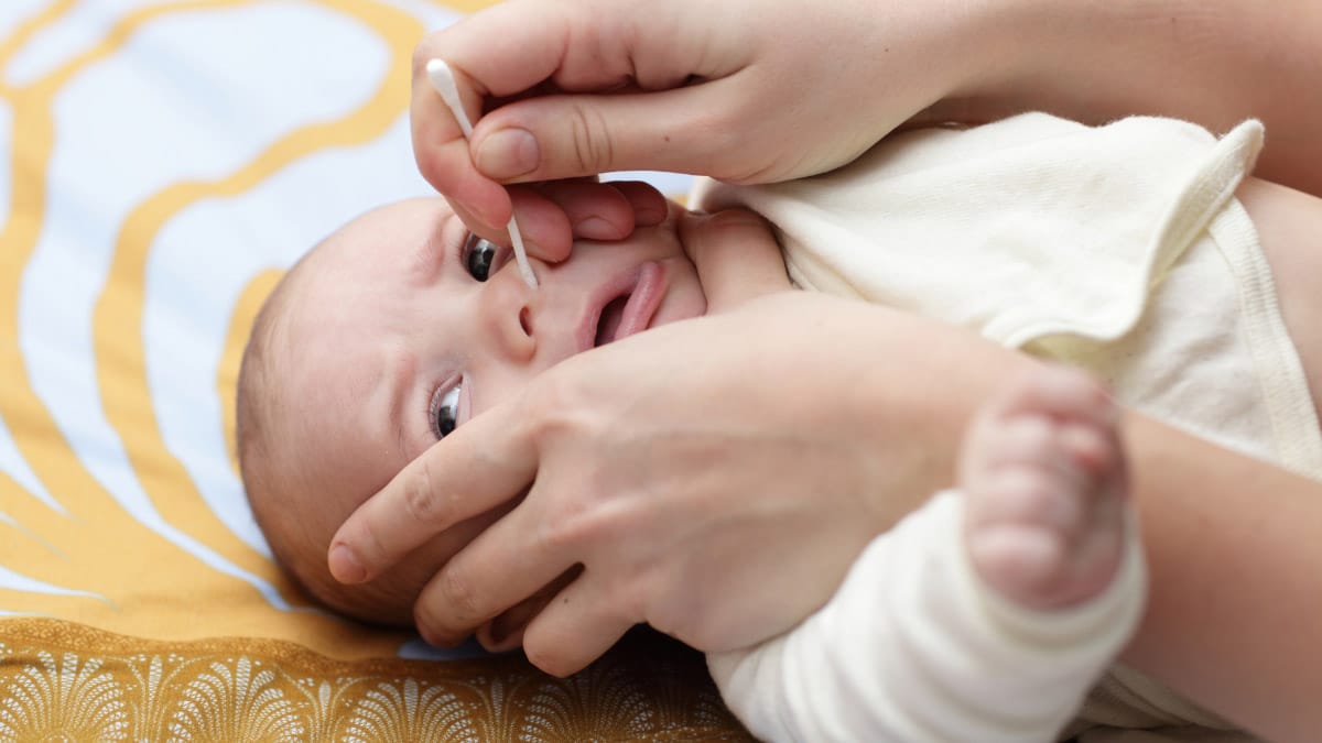 adult hands holding a baby's face and inserting a q-tip in its nose