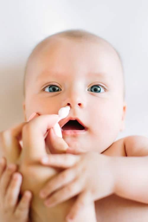 cute baby having its nose cleaned with a safety Q-tip