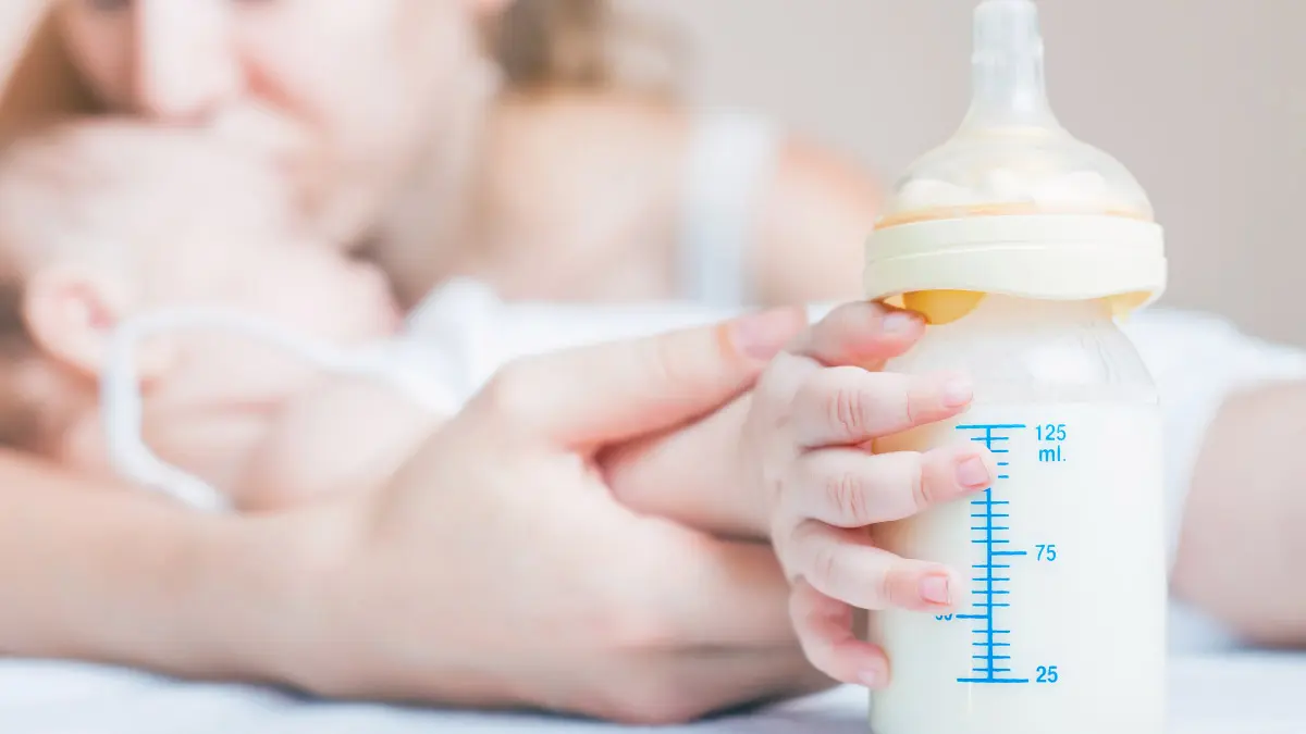 mother kissing her baby, whose hand is holding a pumped bottle of breast milk