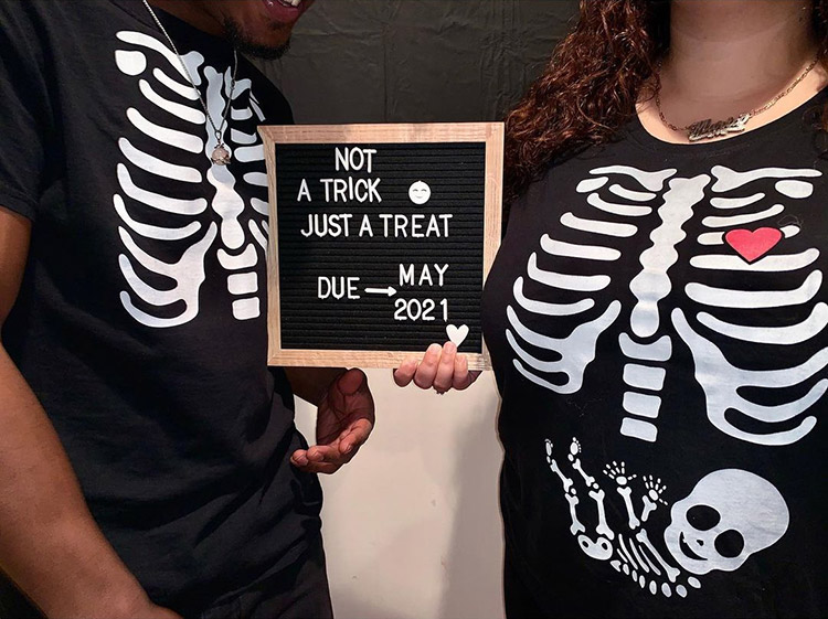couple in x-ray shirts with the woman's featuring a skeleton baby in the stomach. she's holding a sign that says "not a trick, just a treat, due May 2021"