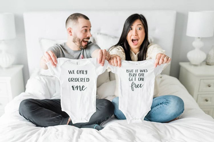 couple holding up two onesies that read "we only ordered one" and "but it was buy one get one free" to show they're pregnant with twins