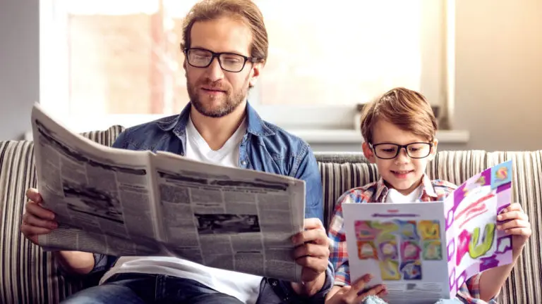 father and son both wearing glasses and reading a newspaper and magazine while sitting on the couch