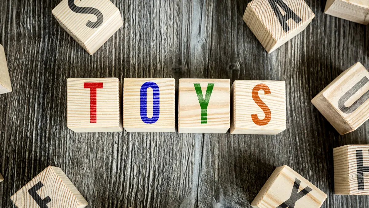 wooden letter blocks spelling out TOYS on a dark wood table