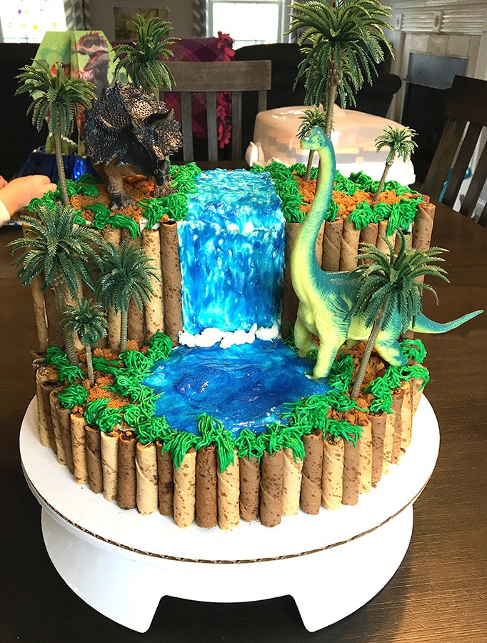 a dinosaur cake with a waterfall coming down a cliff into a plunge pool