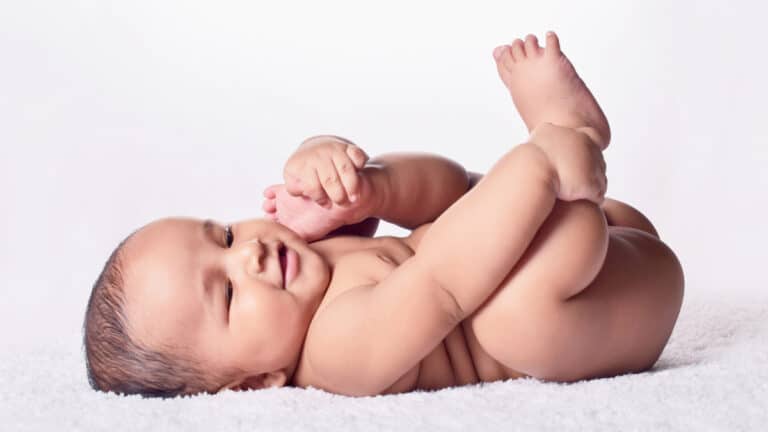 naked baby boy lying on a blanket raising his feet in the air